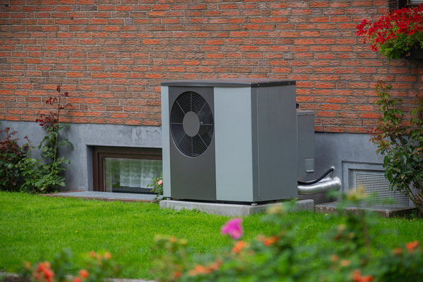 „Effiziente Außeneinheit einer Wärmepumpe auf einem stabilen Betonfundament neben einem Backsteinhaus, umgeben von gepflegter Grünfläche. Symbolisiert nachhaltige Heizlösungen und energieeffiziente Gebäudetechnik in der modernen SHK-Branche. - © snapshotfreddy - stock.adobe.com