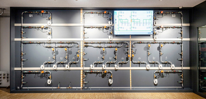 An der Wand montiertes Netz von Leitungen und Messgeräten mit einem großen Monitor, der ein Diagramm über dem System anzeigt. - © Bild: Geberit